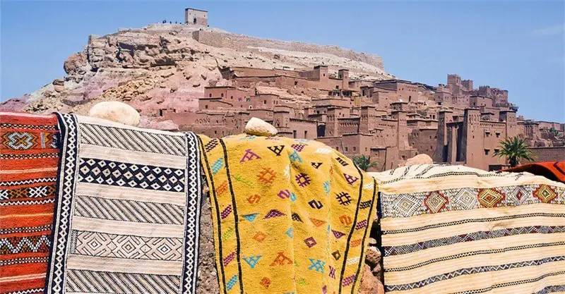 Colourful Berber rugs draped before the mud-brick village of Ait Ben Haddou