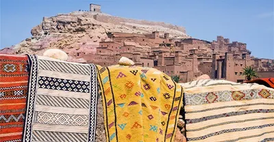 Colourful Berber rugs draped before the mud-brick village of Ait Ben Haddou