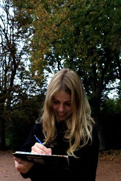 Lee Meneres smiling while writing in a notebook outdoors among autumn trees
