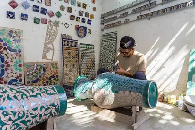 Artisan hand-finishing a geometric ceramic vase in a workshop lined with zellij panels