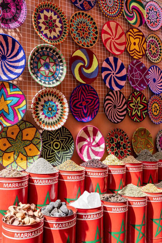 Market stall of patterned woven baskets above red Marrakech spice bins