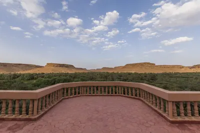 View from a terracotta terrace over a dense palm oasis and flat-topped desert mesas