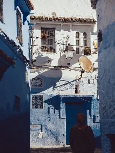 Person walking through a sunlit blue-and-white alley in the Chefchaouen medina