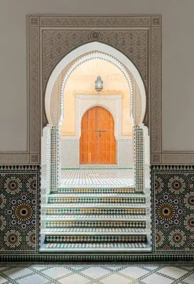 Horseshoe arch of carved plaster and zellij tiles framing a wooden door beyond tiled steps