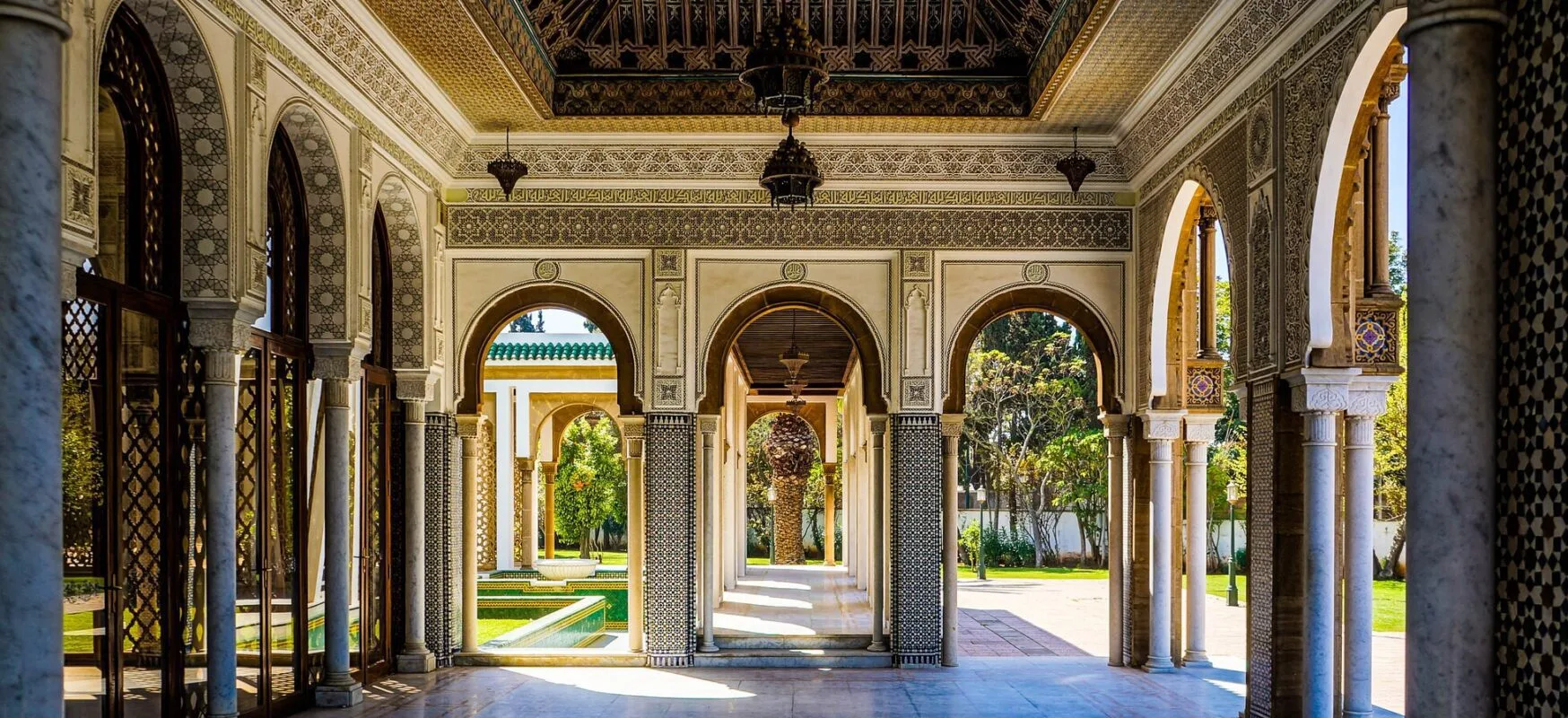 Ornate horseshoe arches with carved plaster and zellij opening onto a sunlit courtyard garden