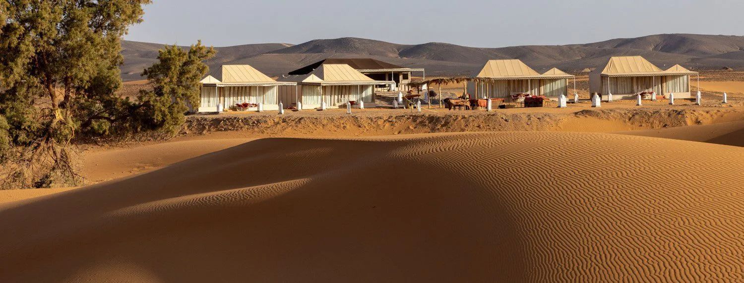Luxury canvas tents on a dune ridge with rippled Sahara sand in the foreground