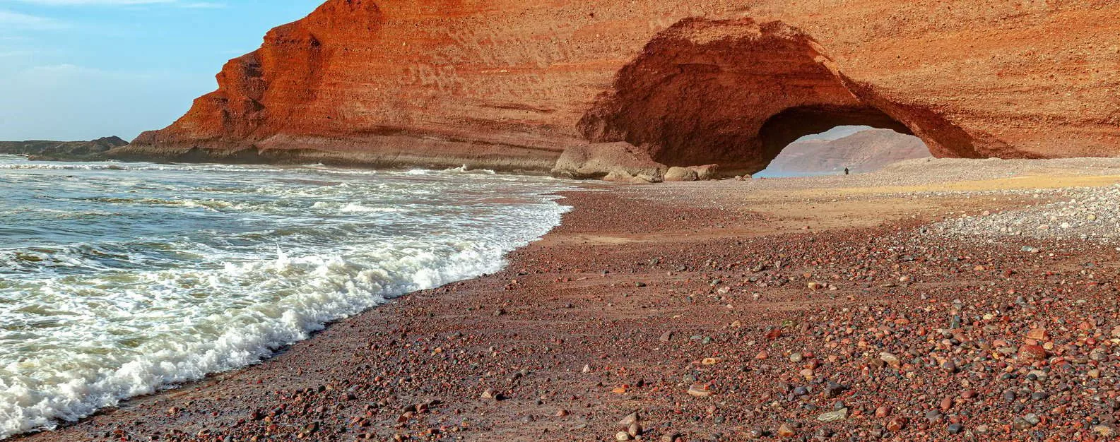 Natural red sandstone arch spanning the pebble beach at Legzira as surf washes ashore