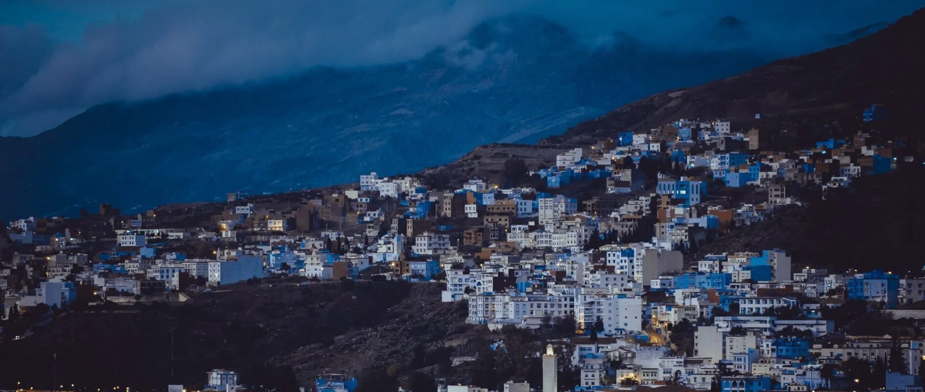 Blue-and-white houses of Chefchaouen climbing a dark mountain slope at dusk