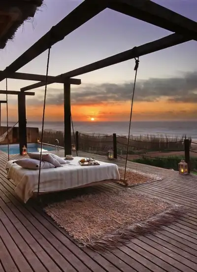 Hanging daybed and lanterns on a wooden terrace overlooking the Atlantic Ocean at sunset