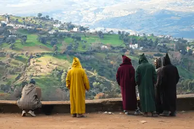 Group in colourful hooded djellabas looking out over a green mountain valley
