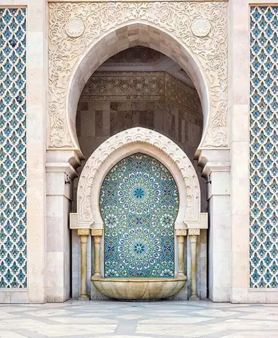 Carved stone mosque fountain set beneath a horseshoe arch of blue zellij mosaic tiles