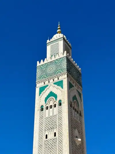 Minaret of the Hassan II Mosque in Casablanca, clad in green zellij tiles against a deep blue sky