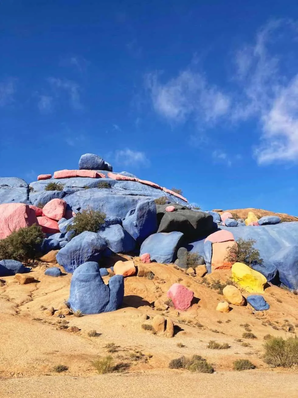 Granite boulders near Tafraoute painted blue, pink and yellow against an arid hillside