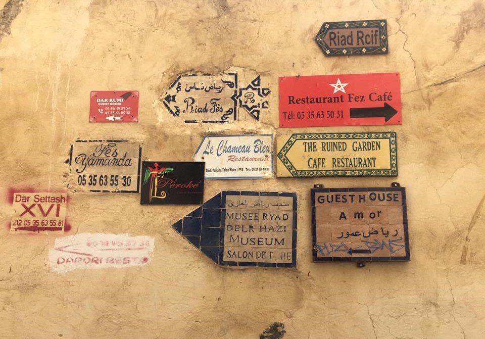 Hand-painted signs for riads, guesthouses and restaurants clustered on a medina wall in Fez