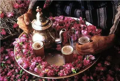 Silver teapot and mint tea glasses nestled among pink rosebuds on a serving tray