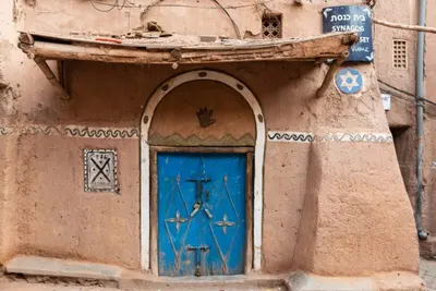 Bright blue synagogue door set in mud-brick walls with Hebrew and English signage