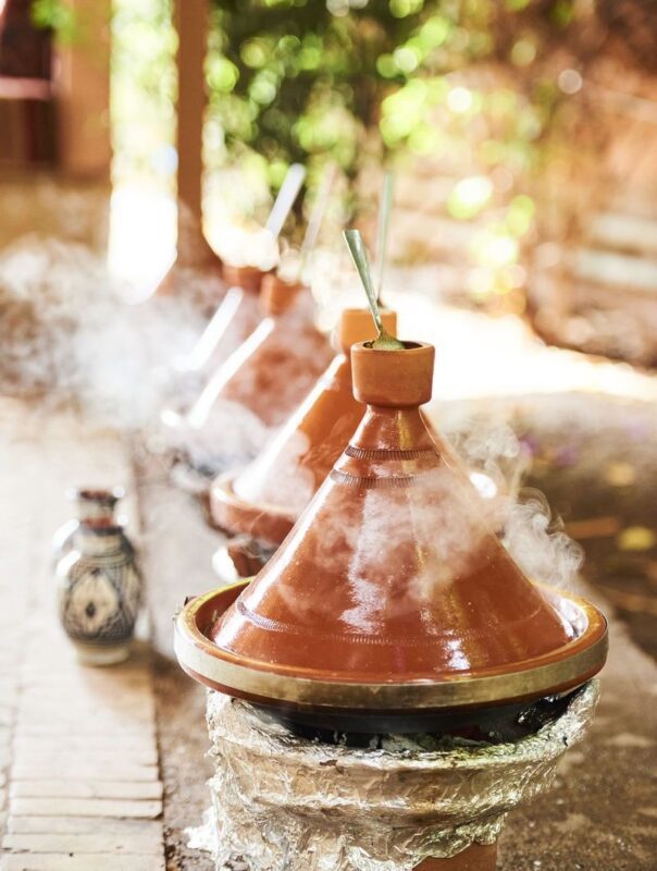 Row of steaming terracotta tagines cooking outdoors on foil-wrapped charcoal burners